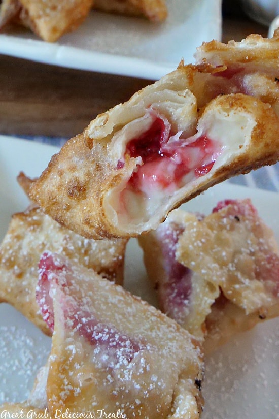 A close up picture of Raspberry Cream Cheese Wontons on a white plate with a bite taken out of one wonton, showing the cream cheese raspberry filling.