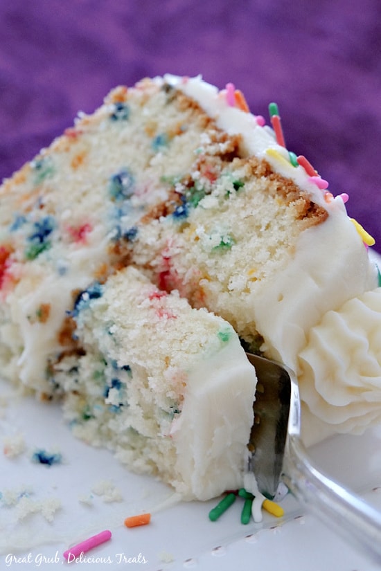 A slice of funfetti cake placed on a white plate laying on it's side with a fork getting ready to scoop up a bite.