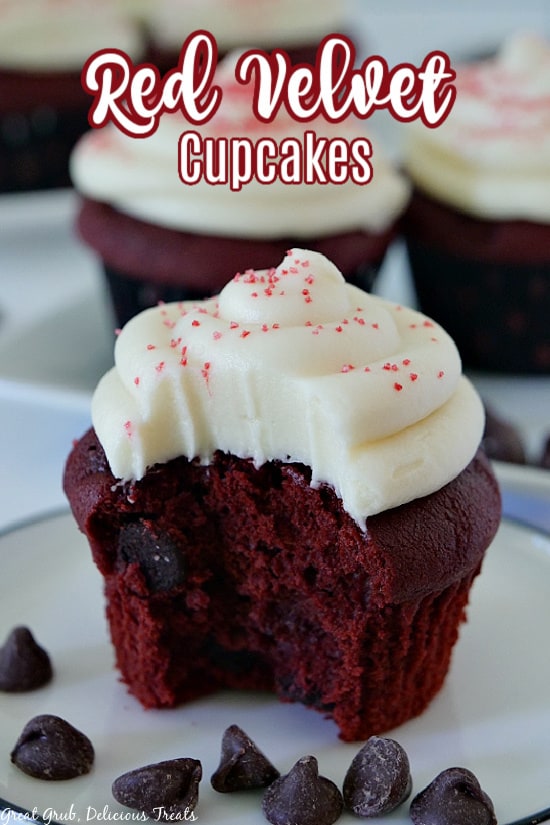 A close up photo of a red velvet cupcake with cream cheese frosting with a bite taken out of it sitting on a white plate with 4 other cupcakes in the background.