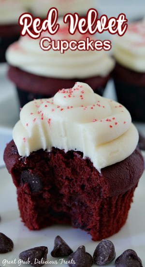 A close up photo of a red velvet cupcake with cream cheese frosting placed on a white plate with more cupcakes in the background.