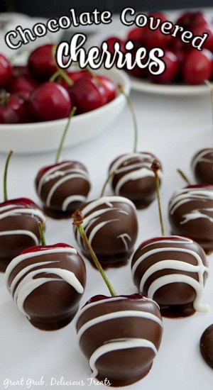 Chocolate covered cherries lined up on a white plate, with two small white bowls of cherries in the background.