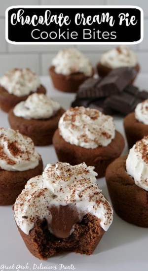 A white surface with Chocolate Cream Pie Cookie Bites placed on it with one of the cookie bites with a bite taken out of it and the title of the recipe at the top of the photo.