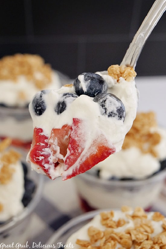 A spoonful of strawberry blueberry parfaits covered in homemade whipped cream and granola.