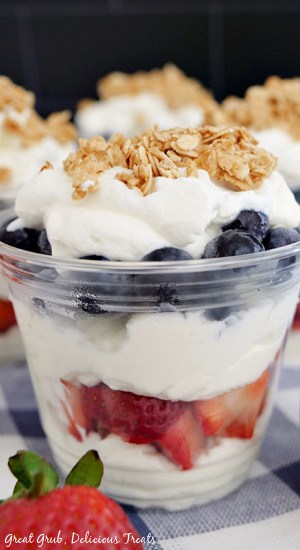 A plastic cup with layers of whipped cream, strawberries, blueberries, and topped with granola.