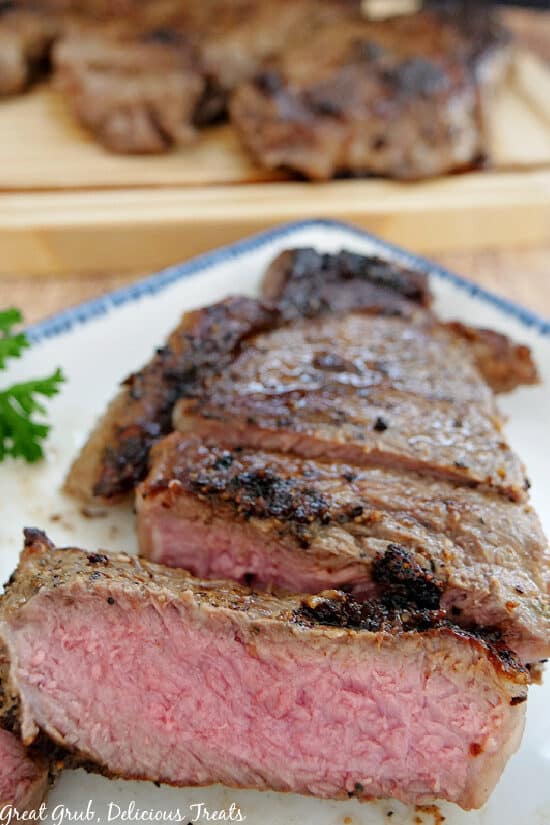 A New York Strip Steak on a white plate with blue trim that has been cut into slices showing the medium rare center.