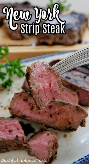 A piece of New York Strip Steak on a fork being held above a white plate with blue trim that has a piece of steak on it that has been cut.