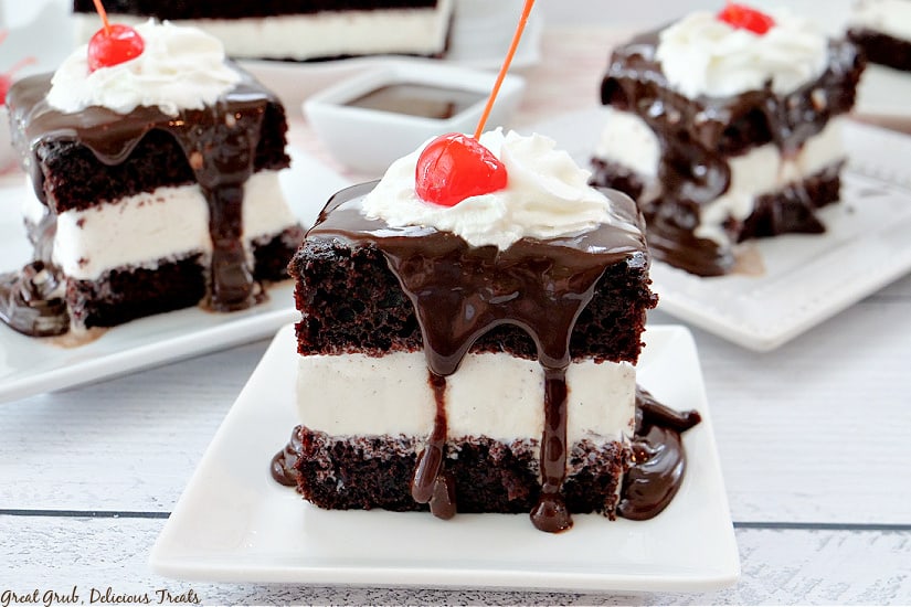 Three white plates with square pieces of hot fudge cake on them, all topped with gooey hot fudge, whipped cream, and a cherry on top.