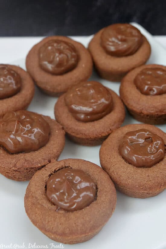 A white surface with 8 chocolate cream pie cookie bites on it before they are topped with whipped cream.