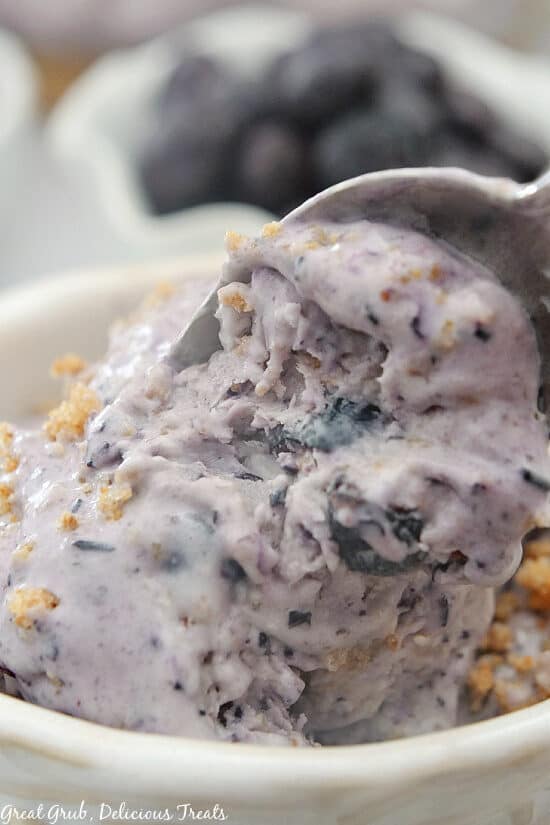 A close up photo of a bowl of blueberry cobbler frozen dessert with a spoon starting to scoop out a bite.