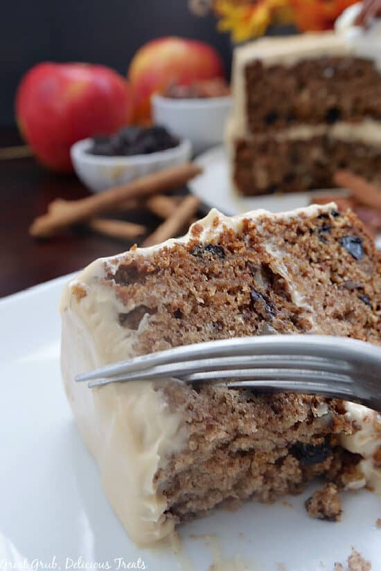 A slice of apple spice cake on a white plate with a fork pressing into the cake to remove a bite.
