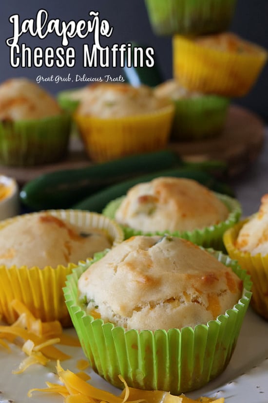 A close up of Jalapeno Cheese Muffins in green and yellow muffin liners with jalapenos in the background.