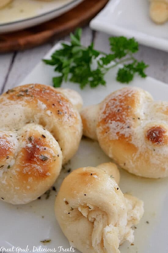 A white plate with 3 garlic knots on it with one having a bite taken out of it.
