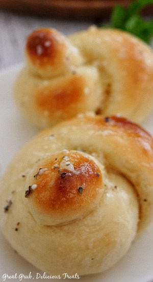 A close up photo of two garlic knots on a white plate.