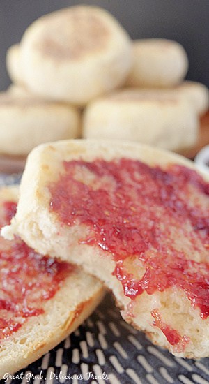 A blue plate with 2 halves of an English muffin on it with jelly on top and a brown plate with muffins on it in the background.