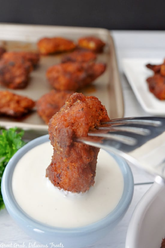 A buffalo chicken nugget on a fork being dipped into a light blue bowl filled with ranch dressing.
