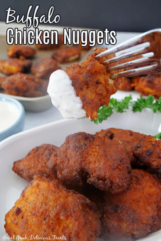 A buffalo chicken nugget on a fork that has been dipped in ranch dressing being held above a white plate with more nuggets on it.