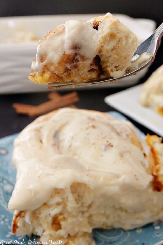 A close up photo of a fork with a bite of pumpkin spice cinnamon roll on it being held above the whole cinnamon roll.