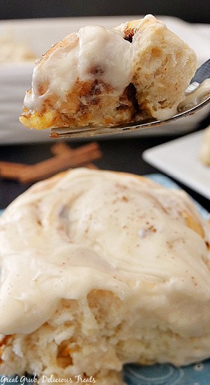 A close up photo of a bite of pumpkin spice cinnamon roll on a fork held above the whole cinnamon roll.