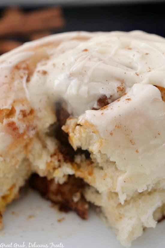 A super close up photo of a cinnamon roll on a white plate with a bite taken out of it.