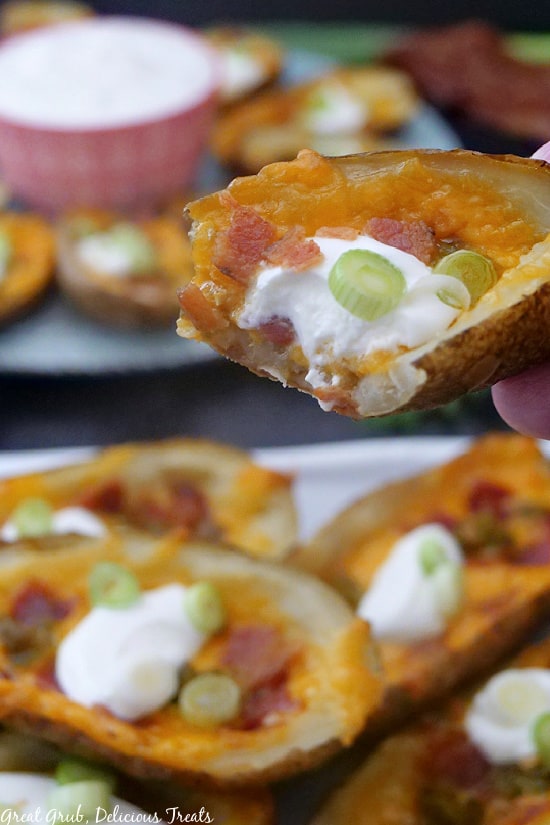 A close up photo of a loaded potato skin with cheese, bacon, sour cream, and chives on top.