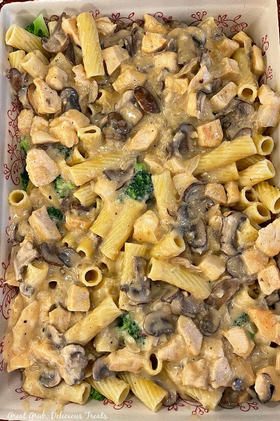 A 13 x 9 baking dish filled with chicken, broccoli, pasta, cheese, mushrooms all in a creamy sauce.