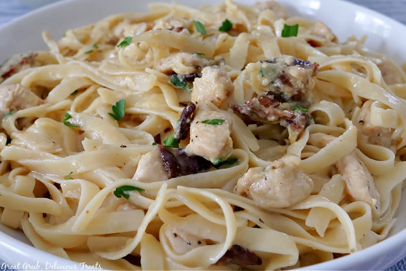 A large bowl filled with chicken carbonara with chunks of chicken, bacon, and parsley mixed in.