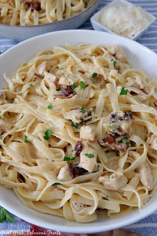 A large white bowl filled with chicken carbonara, chunks of chicken, diced bacon, and sprinkled with parsley.