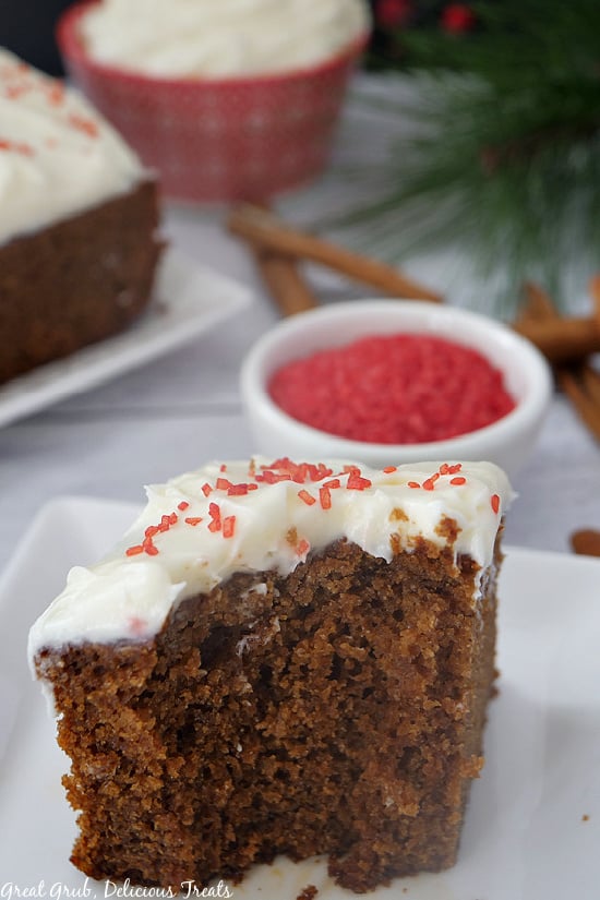 A slice of gingerbread cake on a white plate with frosting and red sprinkles.