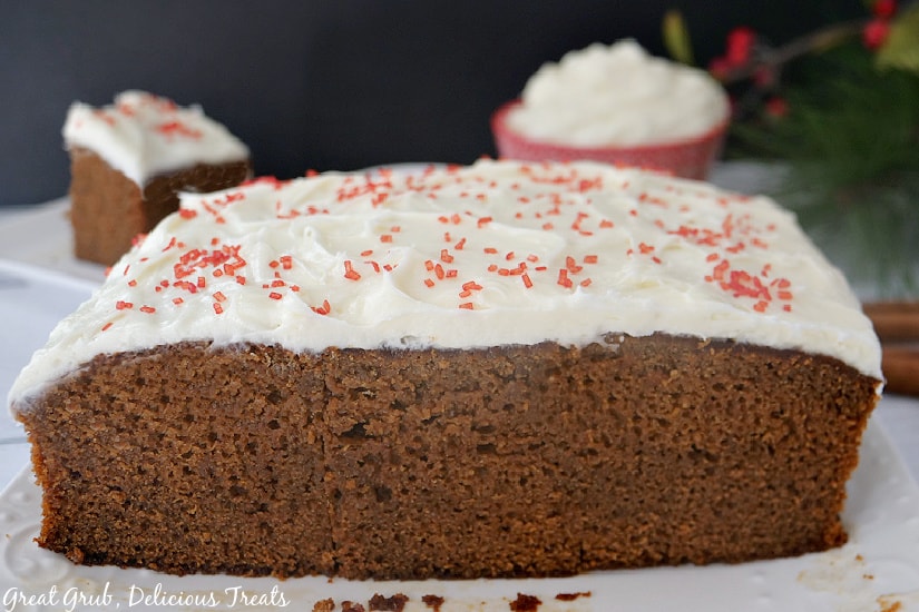 A whole cake on a white plate, topped with cream cheese frosting and tiny red sprinkles.