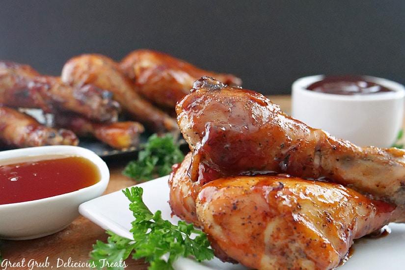 Horizontal picture of Honey Barbecue Chicken drumsticks on a white plate with parsley in the background.