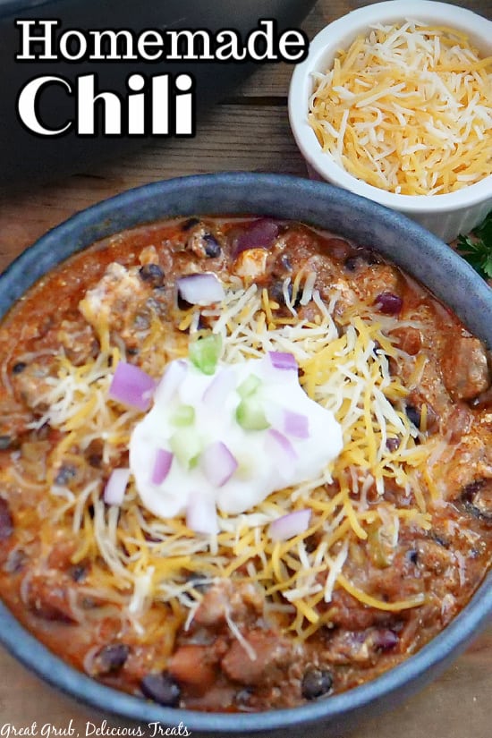 Homemade Chili in a grey bowl with shredded cheese, sour cream, green onions, and red onions on top.