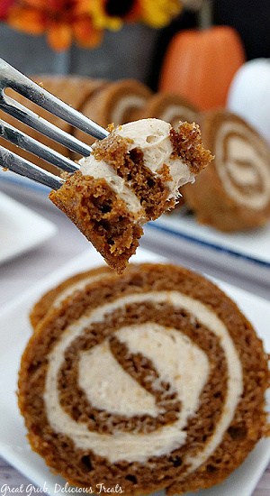 A close up bite of pumpkin roll with a slice on a white plate below.