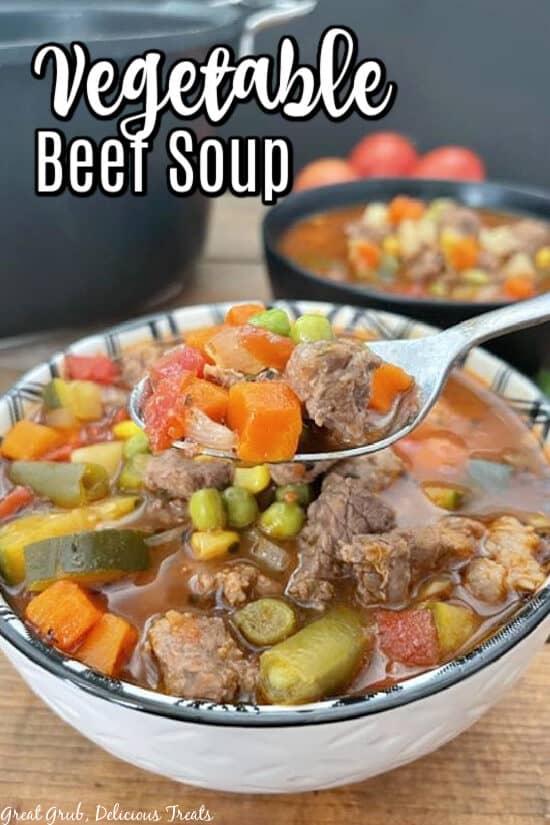 A white and black bowl with homemade vegetable beef soup and a spoon holding up a bite.