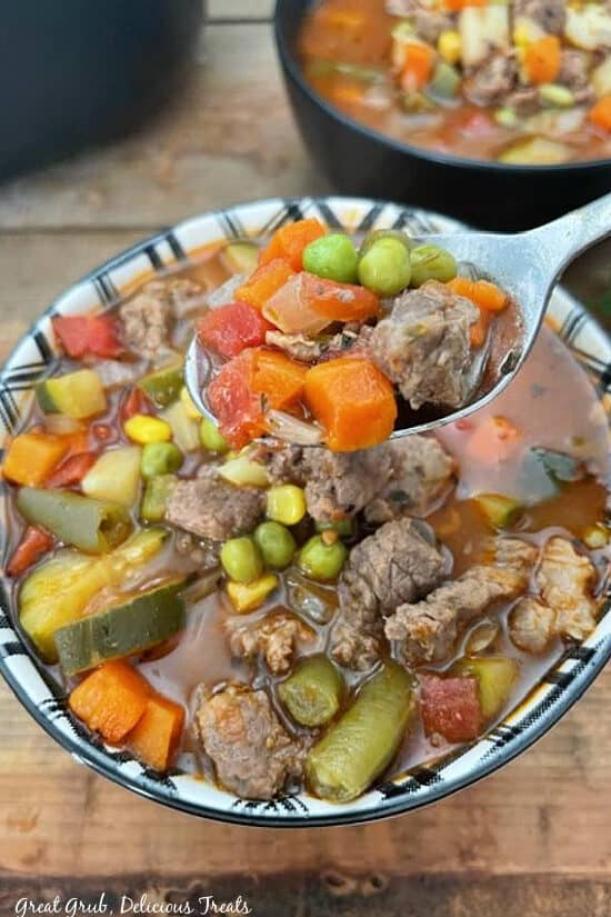 A close up of a spoonful of vegetable beef soup held above a serving bowl filled with soup.