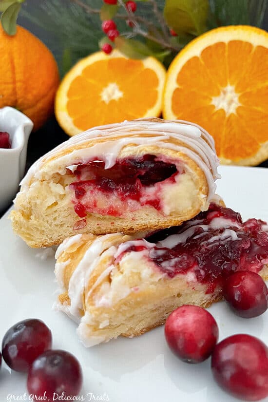 A white plate with a couple slices of cranberry cream cheese pastry on it with oranges in the background.