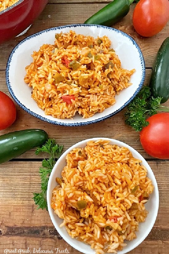 An overhead photo of Spanish Rice placed in two bowls, with tomatoes, jalapenos, and parsley in the background.