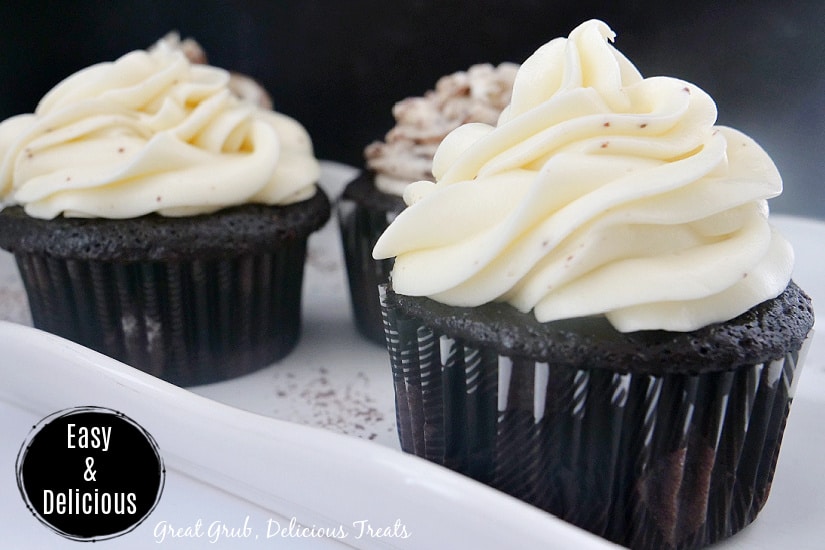 Three chocolate cupcakes with buttercream frosting on a white tray.