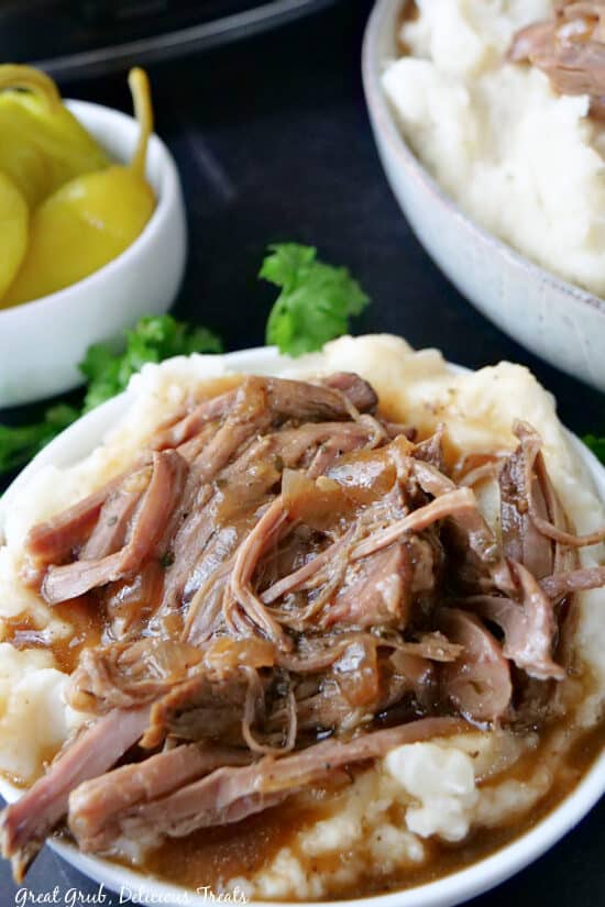 A close up photo of a white bowl filled with Mississippi Pot Roast served over mashed potatoes.