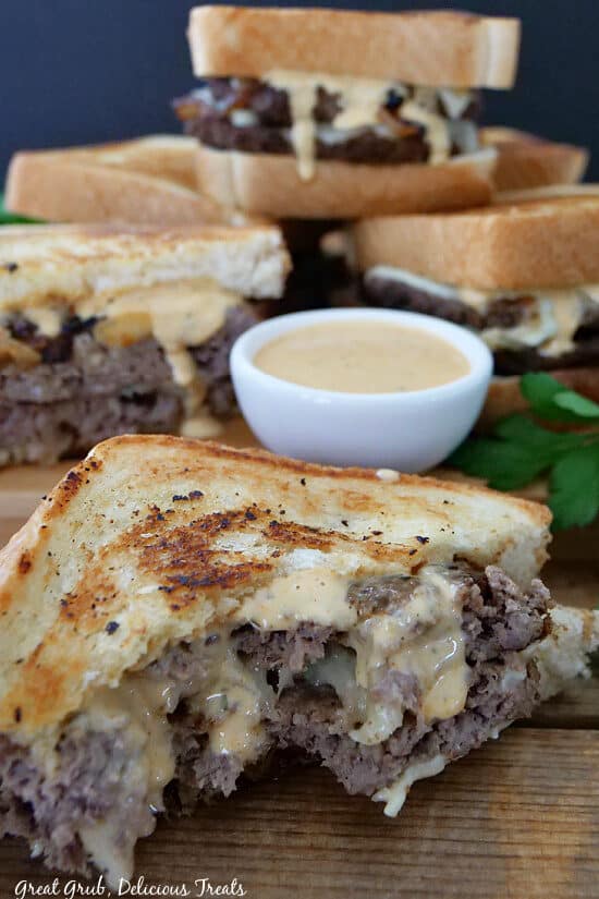 Patty Melt sandwiches on a wooden board with a white small bowl of creamy secret sauce.