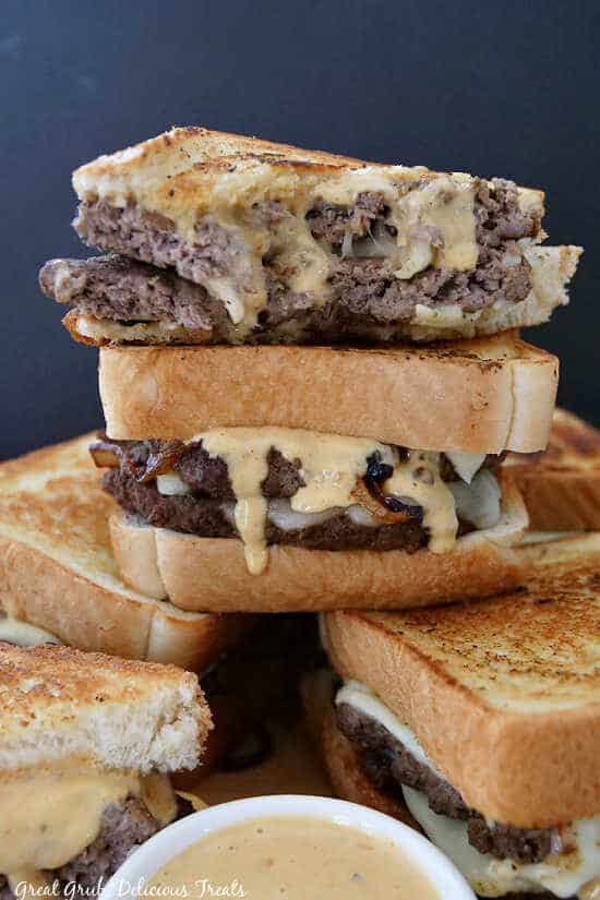 A stack of patty melts with a small white bowl of creamy sauce.