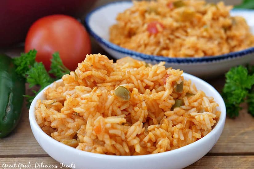 A large bowl of Spanish rice sitting in front of tomatoes and jalapenos.
