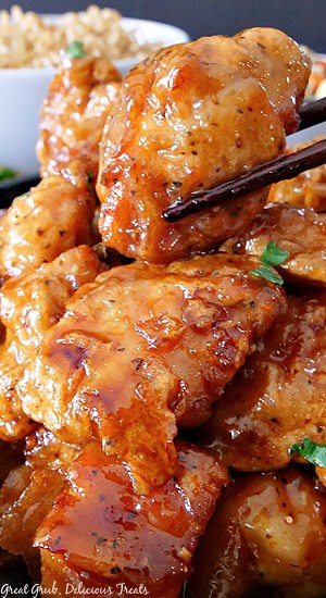 A super close up of a piece of orange chicken being held with chopsticks.