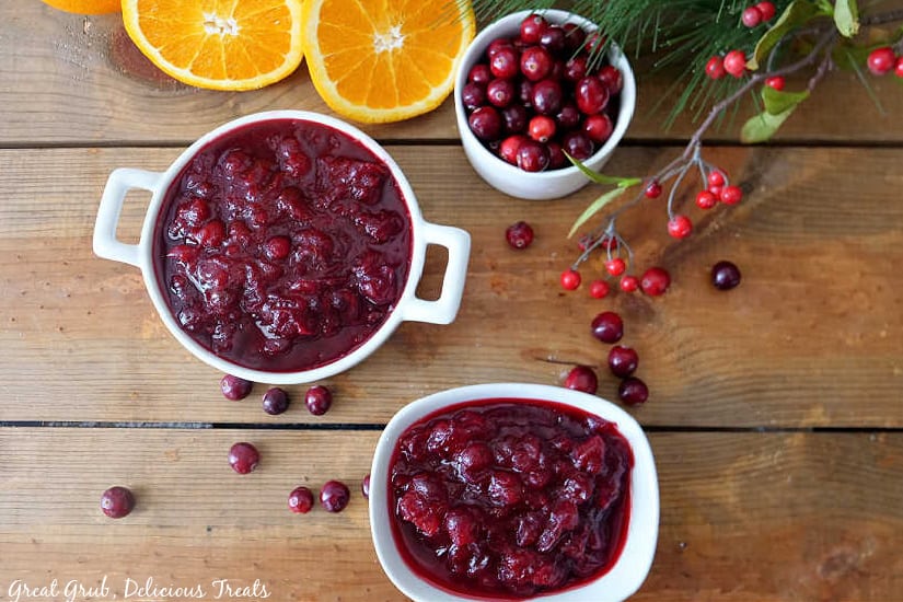 A wood surface with three white bowls, 2 filled with homemade cranberry sauce and one filled with fresh cranberries.