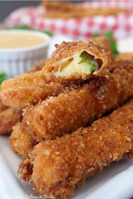 A close up photo of a stack of fried zucchini with a bite taken out of one of them.