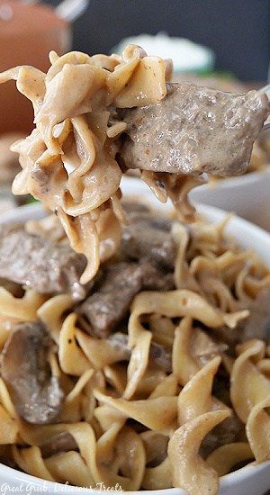A close up photo of a fork with a bite of beef and noodles on it.