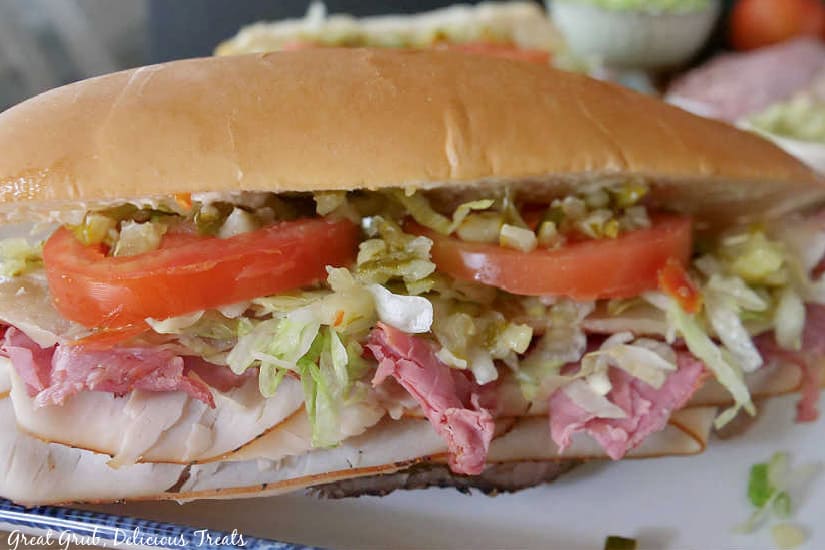 A hoagie roll stuffed with turkey, roast beef, pastrami, provolone cheese, tomatoes, lettuce, and relish.