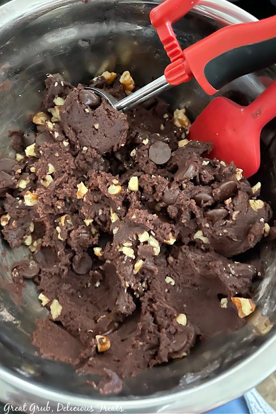 Dark chocolate cookie batter in a mixing bowl with a cookie scoop full of batter sitting inside the bowl.