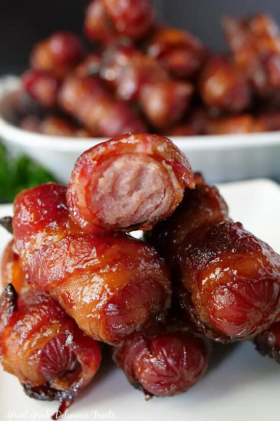 A close up photo of a stack of little smokies wrapped in bacon on a white plate.