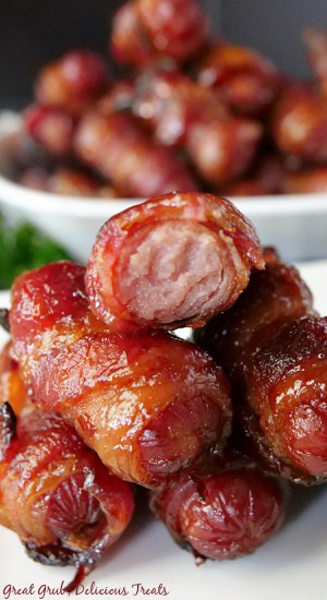 A close up photo of a stack of little smokies wrapped in bacon on a white plate.