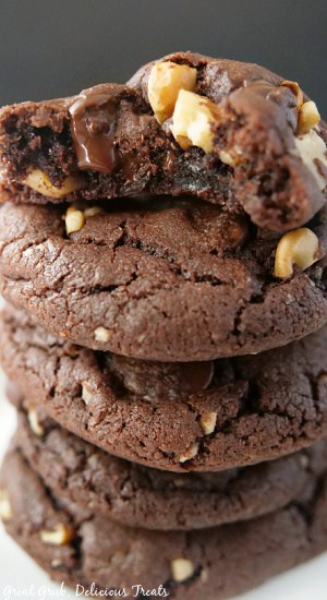 A close up picture of dark chocolate cookies stacked on top of each other with a bite taken out of the top cookie.